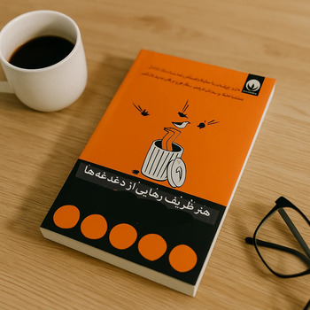 جلد کتاب هنر ظریف رهایی از دغدغه‌ها با زمینه چوب بلوط روشن و فنجان قهوه و عینک مطالعه